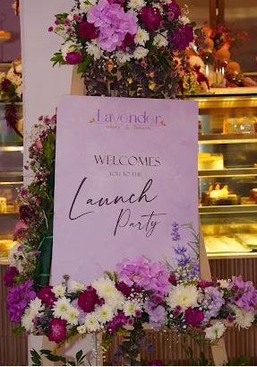Floral arrangement with a 'Lavender' launch party sign in a bakery setting.