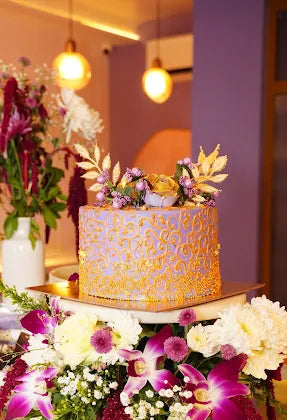 Decorative cake with gold patterns and floral decorations on a table with flowers.